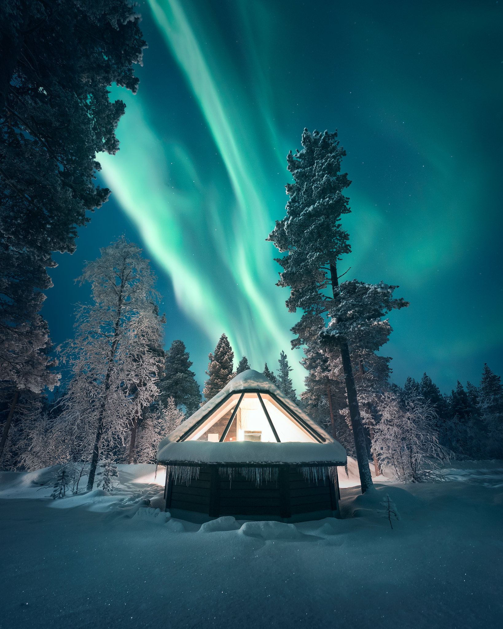 The northern lights over a glass roofed cabin at Aurora Village in Finnish Lapland